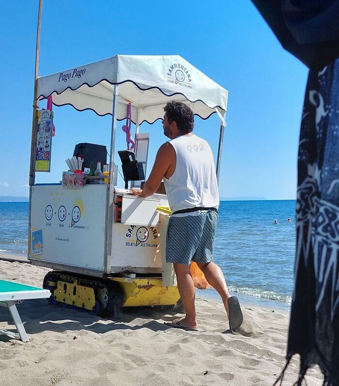 Man operating a beachside ice cream cart, a quirky treasure washed ashore, with the sea in the background.