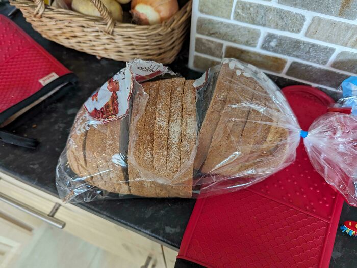 A loaf of sliced bread placed unevenly in a plastic bag, partially open on a kitchen counter.