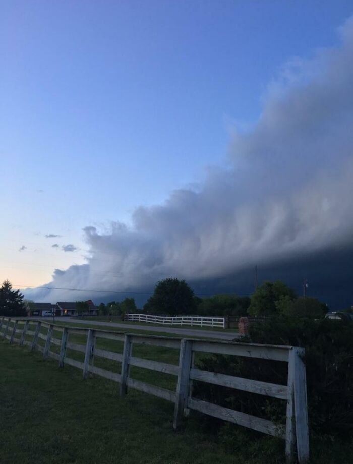 A fascinating cloud shape looms over a rural landscape with an old wooden fence in the foreground.