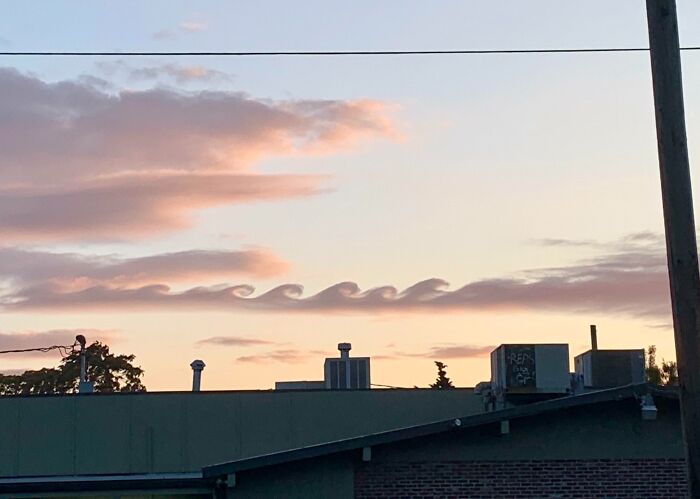 Fascinating cloud shapes resembling ocean waves at sunset above rooftops.