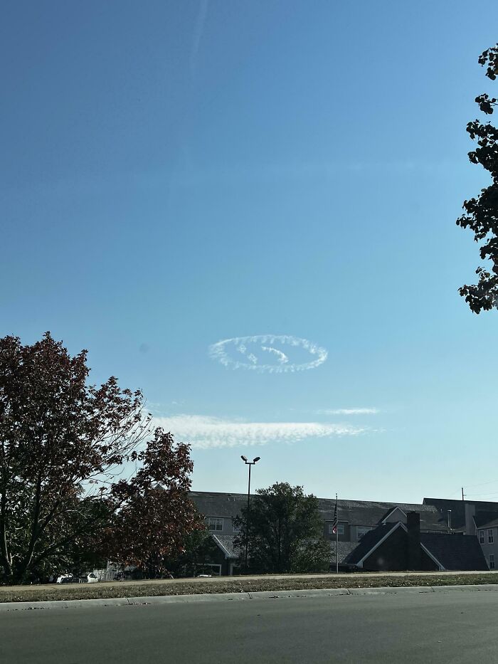 Unusual cloud formation resembling a spiral pattern in the sky above trees and houses.