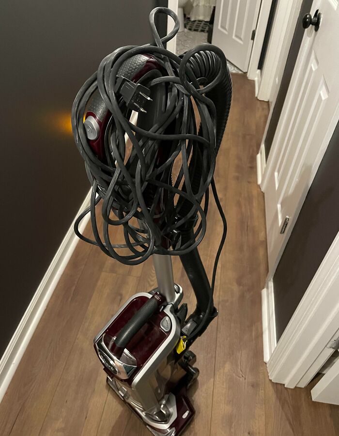 Vacuum cleaner with tangled cord on wooden floor, highlighting infuriating home situations.