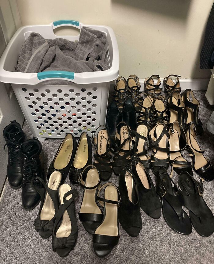 A collection of women's black shoes neatly arranged next to a laundry basket filled with towels.