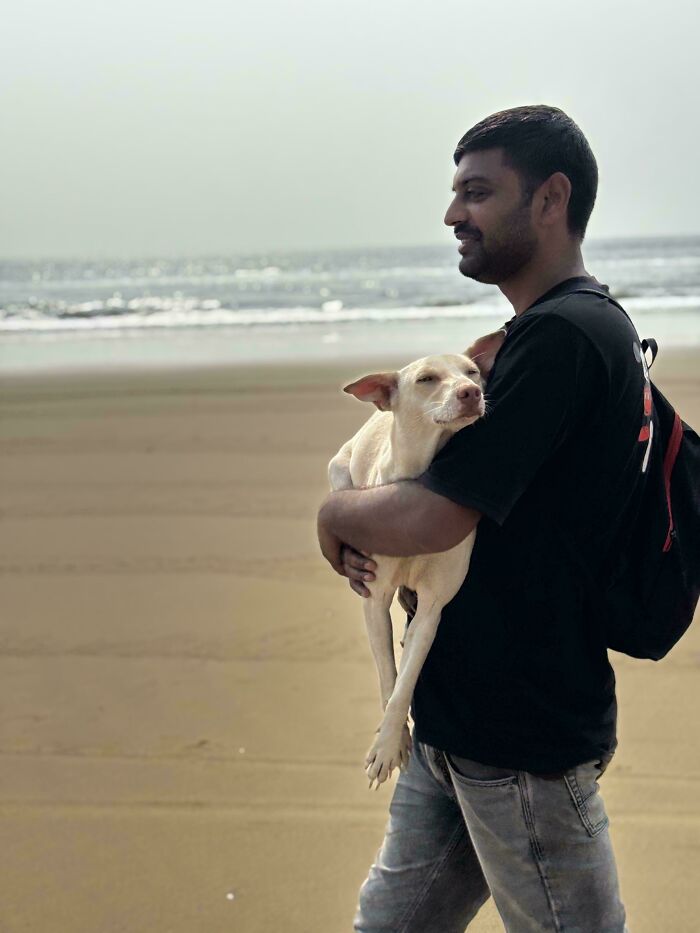 Proud pet owner holding a white dog on a beach, enjoying a sunny day by the sea.