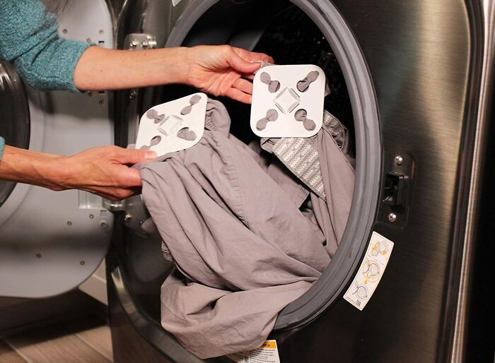 Hands placing affordable home finds on a gray sheet inside a modern front-load washing machine.