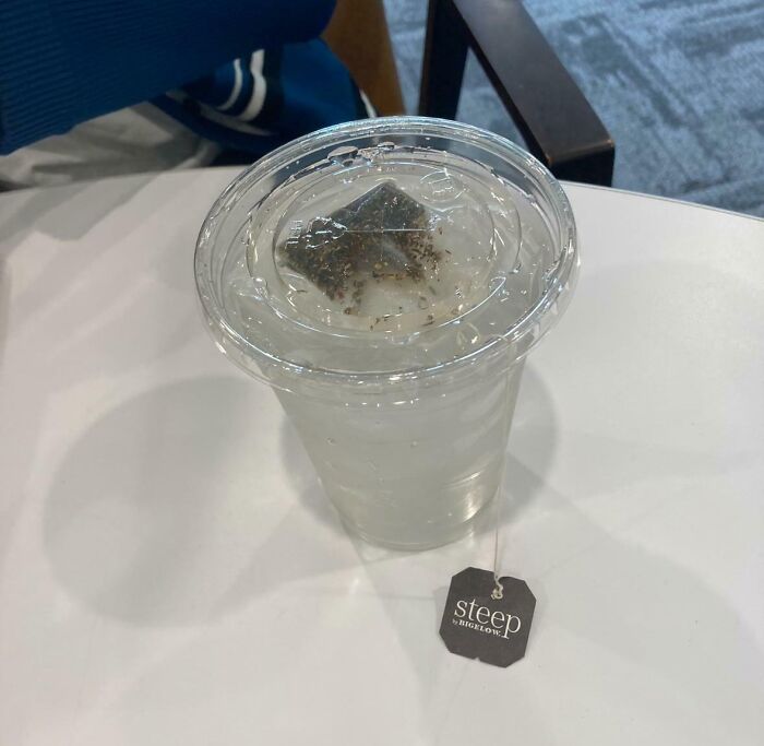 Plastic cup with a tea bag floating in water, highlighting instant regret spending money on a questionable beverage choice.
