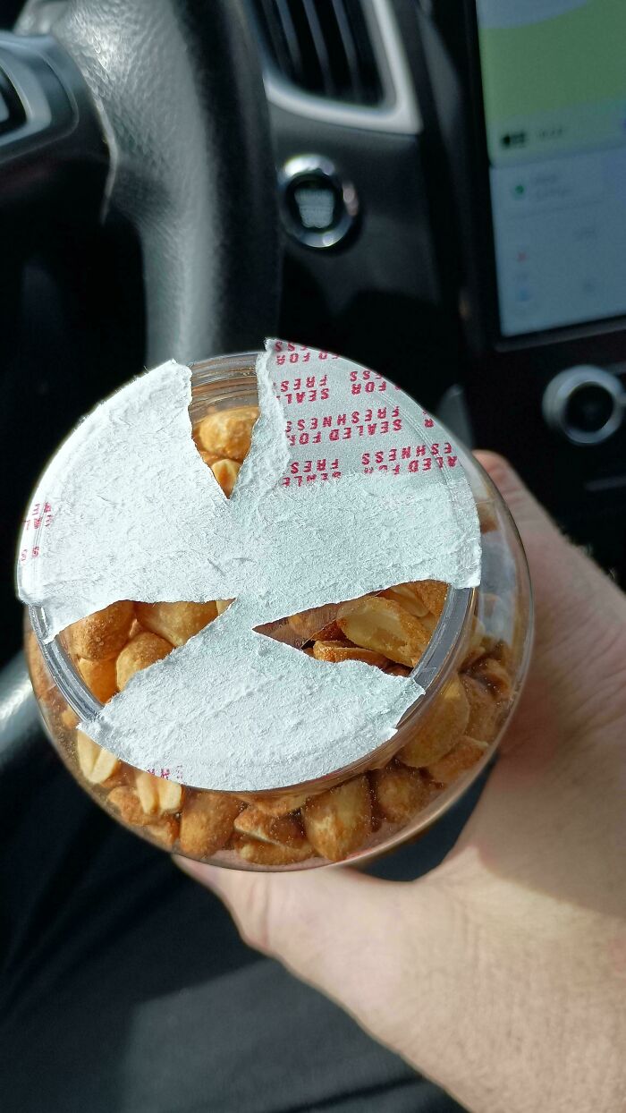 Jar with irritatingly torn seal inside a car, sealing peanuts partially exposed.