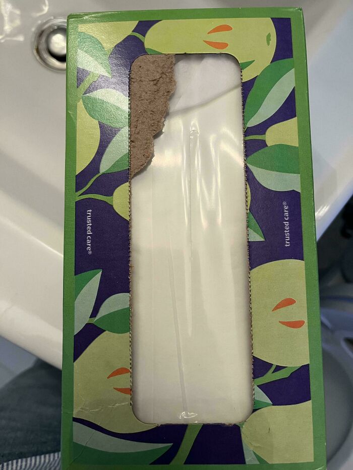Tissue box with cardboard ripped open unevenly, revealing tissues inside.