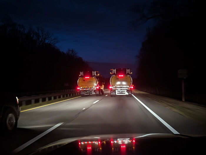 Two trucks blocking highway lanes at night, illustrating people being jerks on the road.
