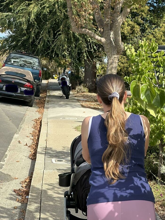 Woman with stroller blocked by inconsiderate parked cars on sidewalk under trees.