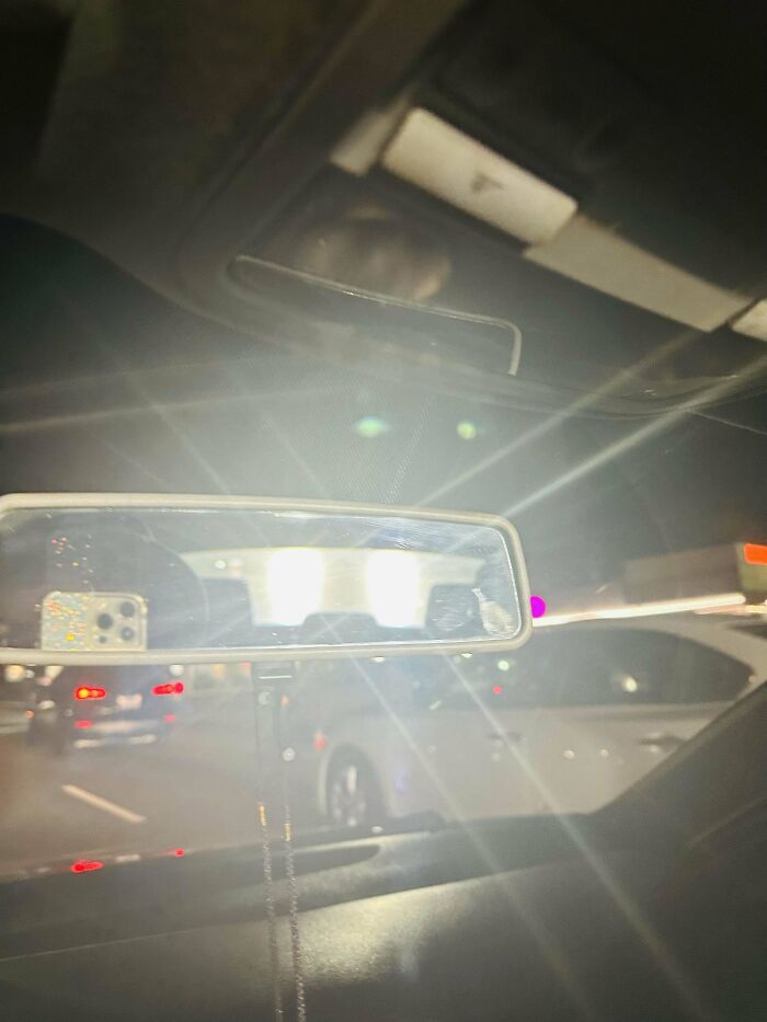 Car driving with high beams on, blinding light in rearview mirror, illustrating people being jerks on the road.