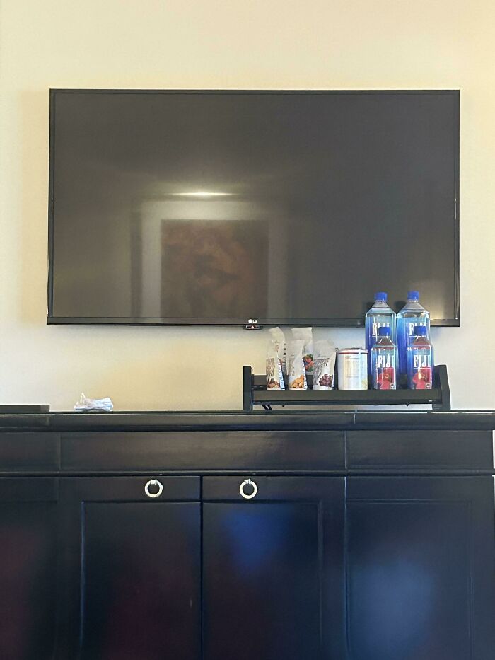 Television in a hotel room with snacks and bottled water placed in front, showcasing people being inconsiderate.