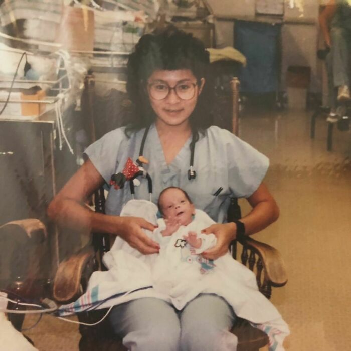 Nurse in '90s hospital room holding a newborn, wearing scrubs and glasses, capturing a wholesome moment.
