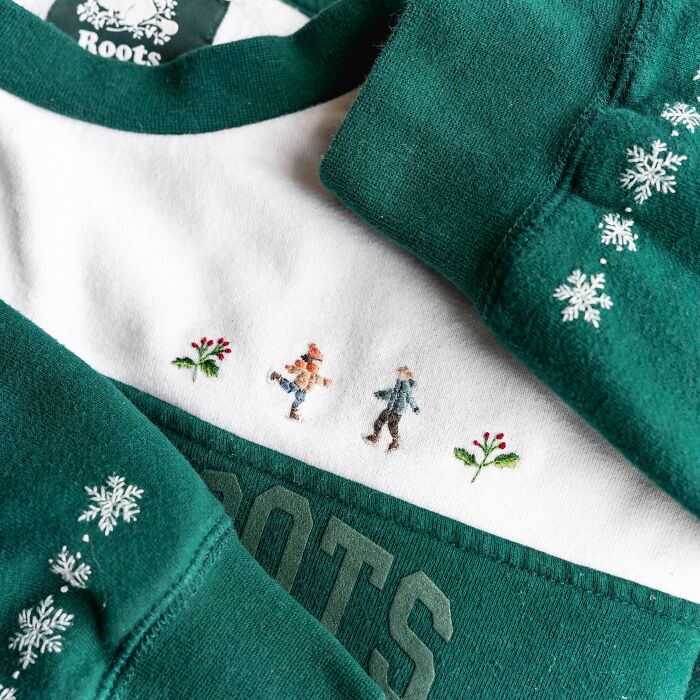 Green and white sweatshirt with detailed embroidery designs of people, flowers, and snowflakes on fabric edges.