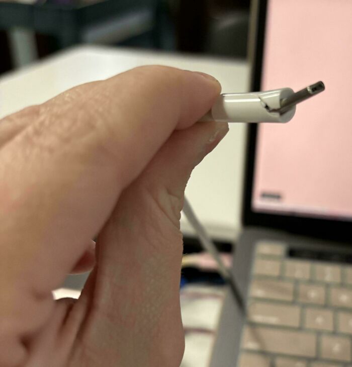 A broken charging cable held in front of a laptop, illustrating frustrating behavior.