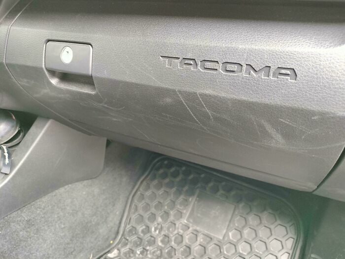 Scratched car glove compartment showing the word 'Tacoma'.