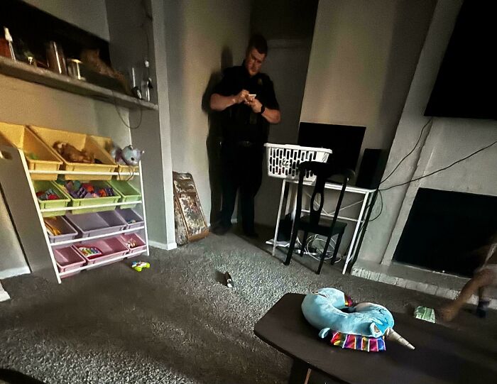 Room with toys scattered, a person standing near a wall looking at a device, capturing a scene of disorder.
