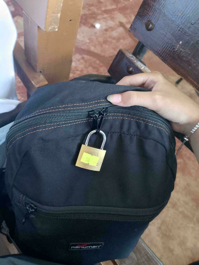 A backpack locked with a padlock on the zipper, someone holding it, illustrating people being jerks.