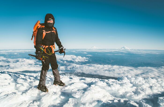 Climber standing on snowy peak with gear, featuring interesting not photoshopped photos under a clear blue sky.