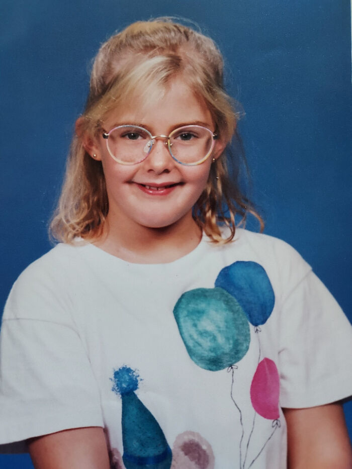 Child in glasses and a balloon shirt during their blunder years, smiling against a blue background.
