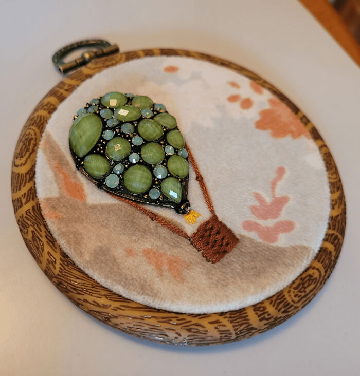 Embroidered hot air balloon adorned with green beads and detailed stitching in a decorative wooden embroidery hoop.