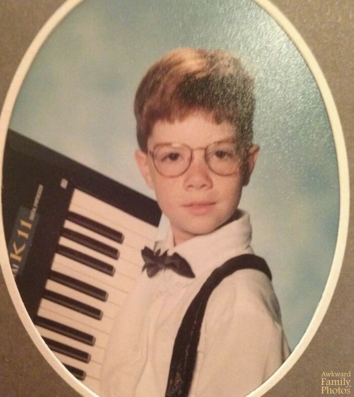 Child with glasses posing with a keyboard, showcasing an awkward family photo.