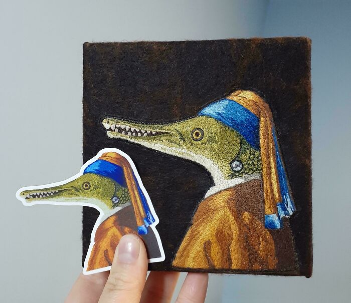 Hand holding embroidered design of a crocodile with blue and orange clothing, showcasing beautiful embroidery designs.