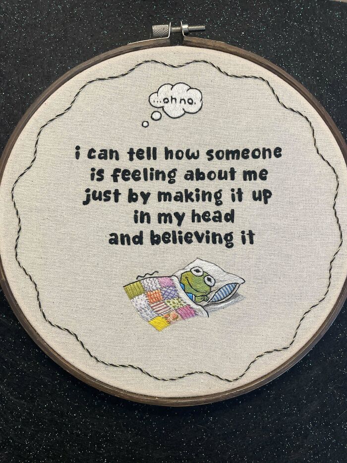 Embroidered hoop art featuring a humorous quote and a small frog tucked in a colorful quilt, showcasing beautiful embroidery designs.