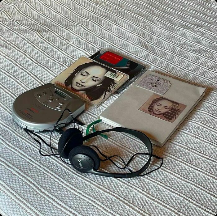 '90s music scene with a portable CD player, Sade album, and headphones on a textured background.