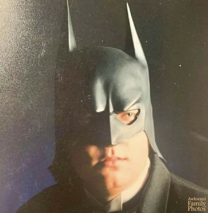 Awkward family photo of a person dressed as Batman with a serious expression.
