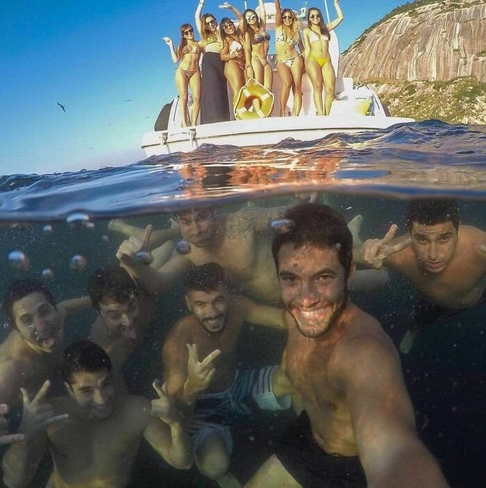 Group of friends having fun, posing underwater near a boat, embodying "pics that go hard" vibes.