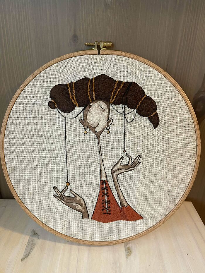 Embroidered art hoop featuring a whimsical figure with intricate hair and delicate thread details in warm tones.