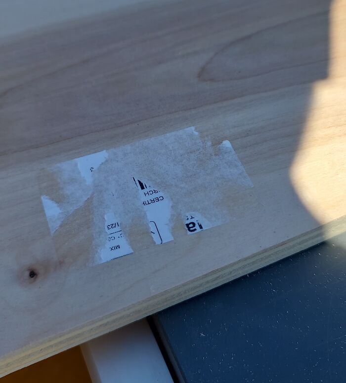 Partially removed sticker on a wooden surface, showcasing an irritating residue mark.