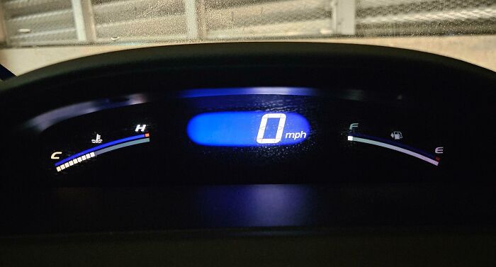 Car dashboard displaying 0 mph, showing fuel gauge almost empty; a mildly infuriating situation for drivers.