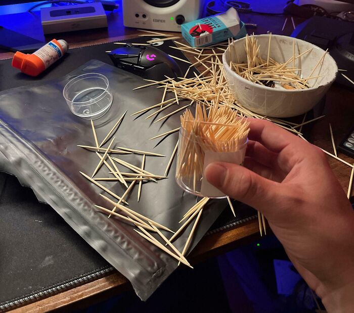 Hand holding a toothpick container with spilled toothpicks on a desk, illustrating irritating things.