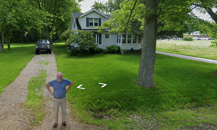 Man on driveway with hands on hips, near a white house, caught on Google Street View.