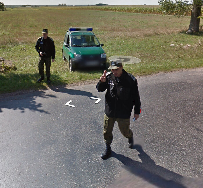 Two officers stand near a green police vehicle on a rural road, captured on Google Street View.