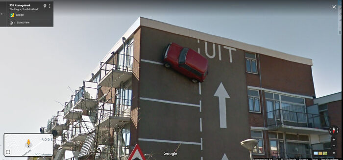 A red car parked vertically on a building wall captured on Google Street View, highlighting a funny life scene.