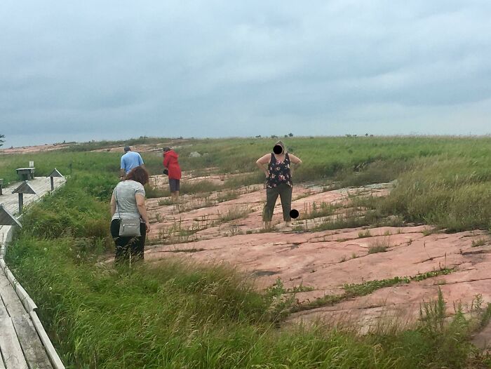 People standing on a protected grass area disregarding signs, illustrating people being jerks in nature.