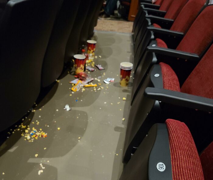 Theater seats with trash and spilled popcorn on the floor, illustrating people being jerks.