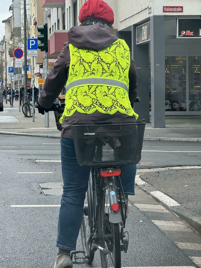 Cyclist wearing a unique bright yellow lace safety vest, exemplifying designers' creativity on city streets.