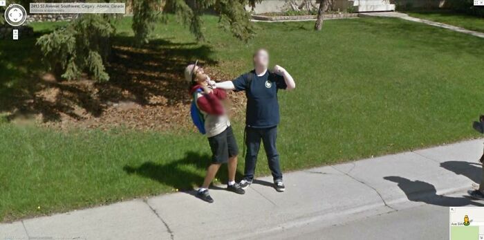 Two people playfully acting on a sidewalk, captured by Google Street View in a quirky life scene.