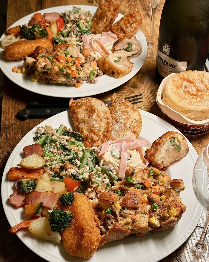 Thanksgiving dinner with diverse dishes, featuring vegetables, stuffing, and rolls on a wooden table.