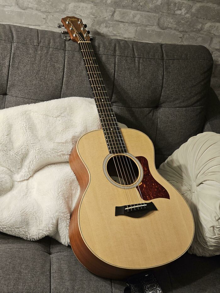 Acoustic guitar resting on a cozy gray sofa with soft pillows, capturing a wholesome Thanksgiving ambiance.