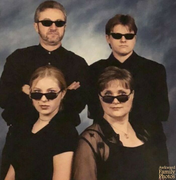 Family posing awkwardly in sunglasses, all wearing black outfits against a blue background.