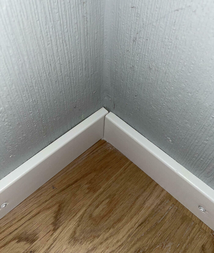 Misaligned corner baseboards showcasing a home improvement fail on wooden flooring.