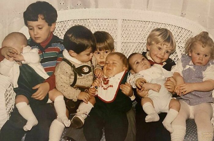 Awkward family photo of young children sitting closely on a white bench.