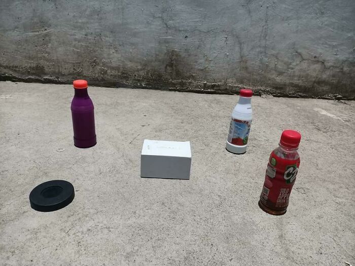 Not photoshopped photo of a clever perspective trick with bottles and a box creating an illusion on a concrete surface.