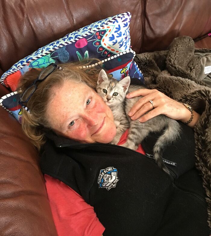 A person smiling with a kitten cuddled on their chest, embodying a wholesome Thanksgiving moment.