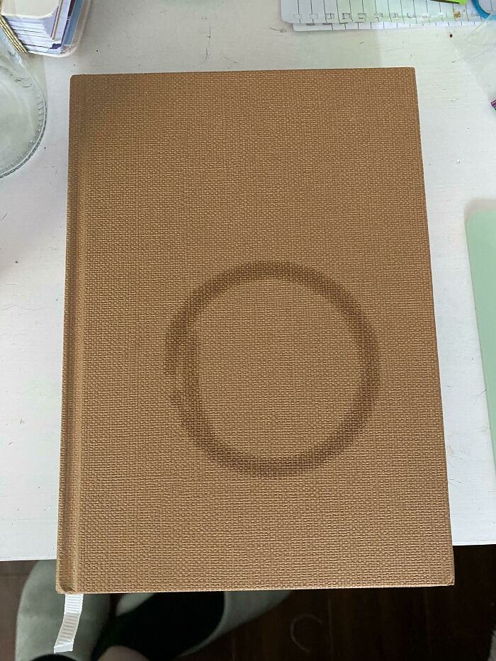 A brown textured book with a circular water stain on the cover, illustrating weaponized incompetence.